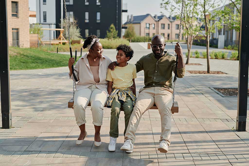 African American family sitting on a swinging bench in a park